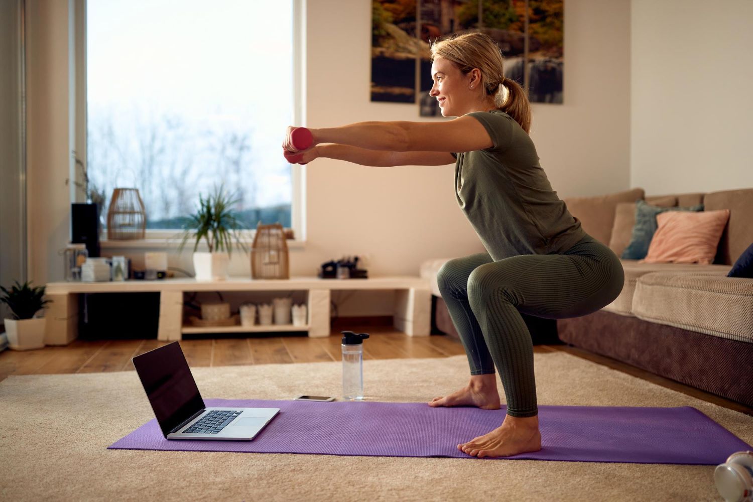 woman in her forties or fifties completing a controlled dumbbell squat in a bright home environment.